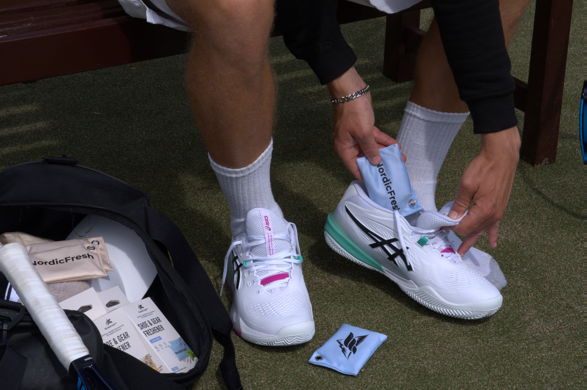 Tennis player inserting a NordicFresh bamboo charcoal shoe freshener pouch into a tennis shoe courtside